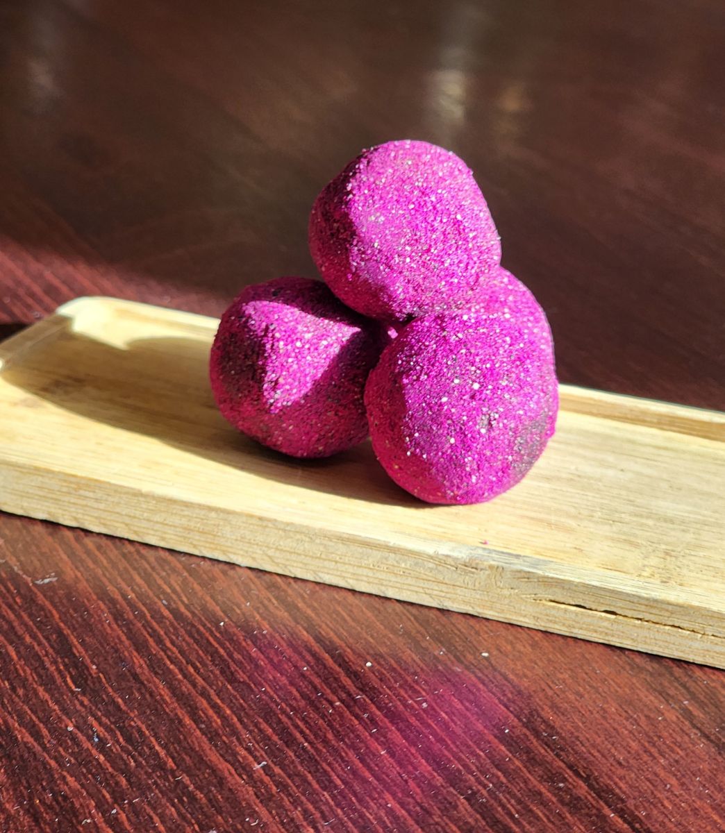 4 magenta tangering dragonfruit chocolate truffles stacked on a wooden plate in the sunlight.