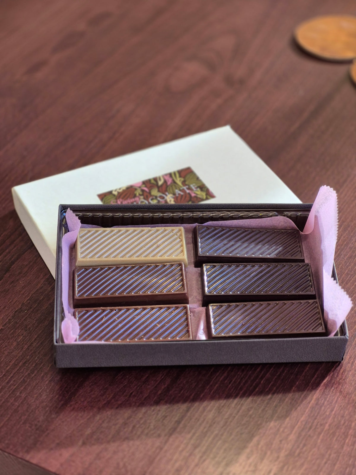 Close-up of six ridged bars in The Connoisseur Box, arranged in two columns on pink tissue beside the white lid.